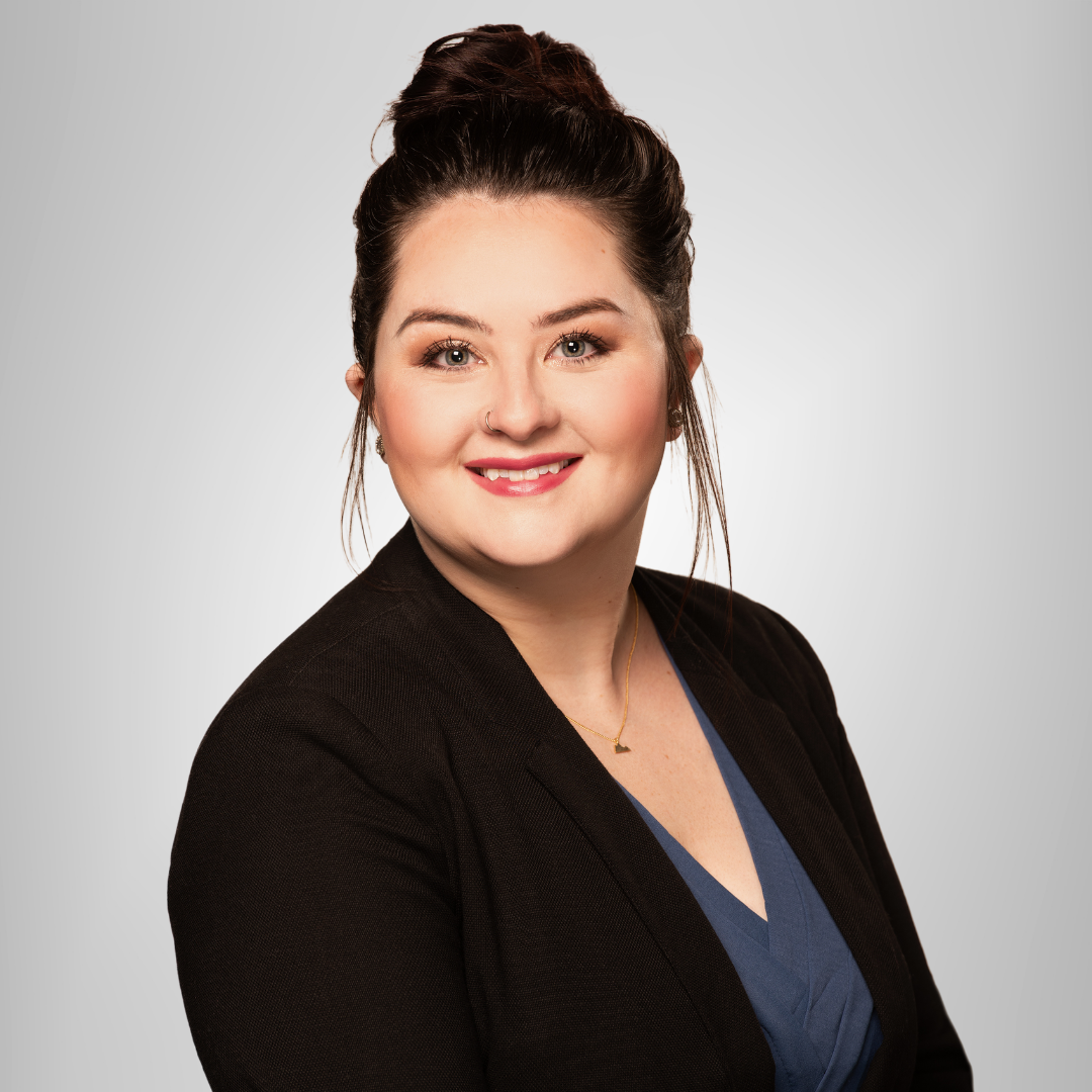 Portrait of a smiling woman in a black blazer and blue top against a light gray background