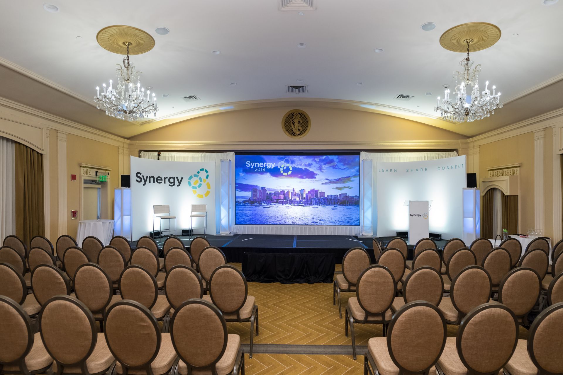 Auditorium set up for a conference. Stage with screen displaying city skyline, rows of chairs.