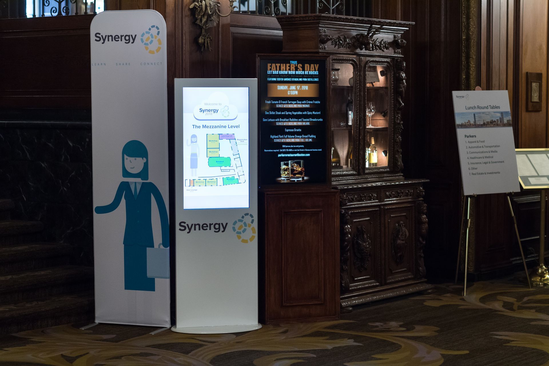 Tall Synergy signs and digital display next to a wooden cabinet. The signs promote the Synergy brand.