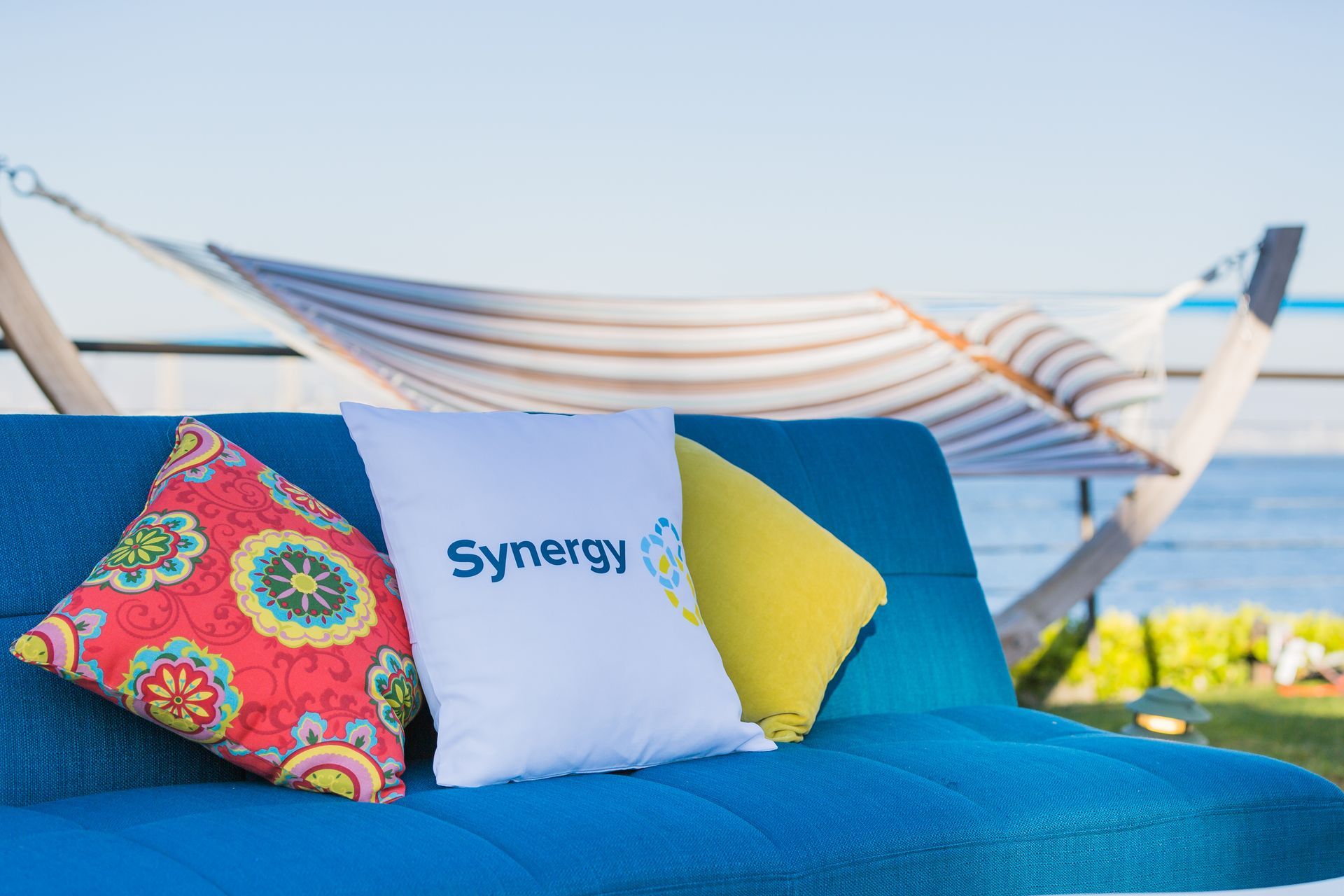 Blue outdoor seating with pillows, Synergy logo, hammock and water view.
