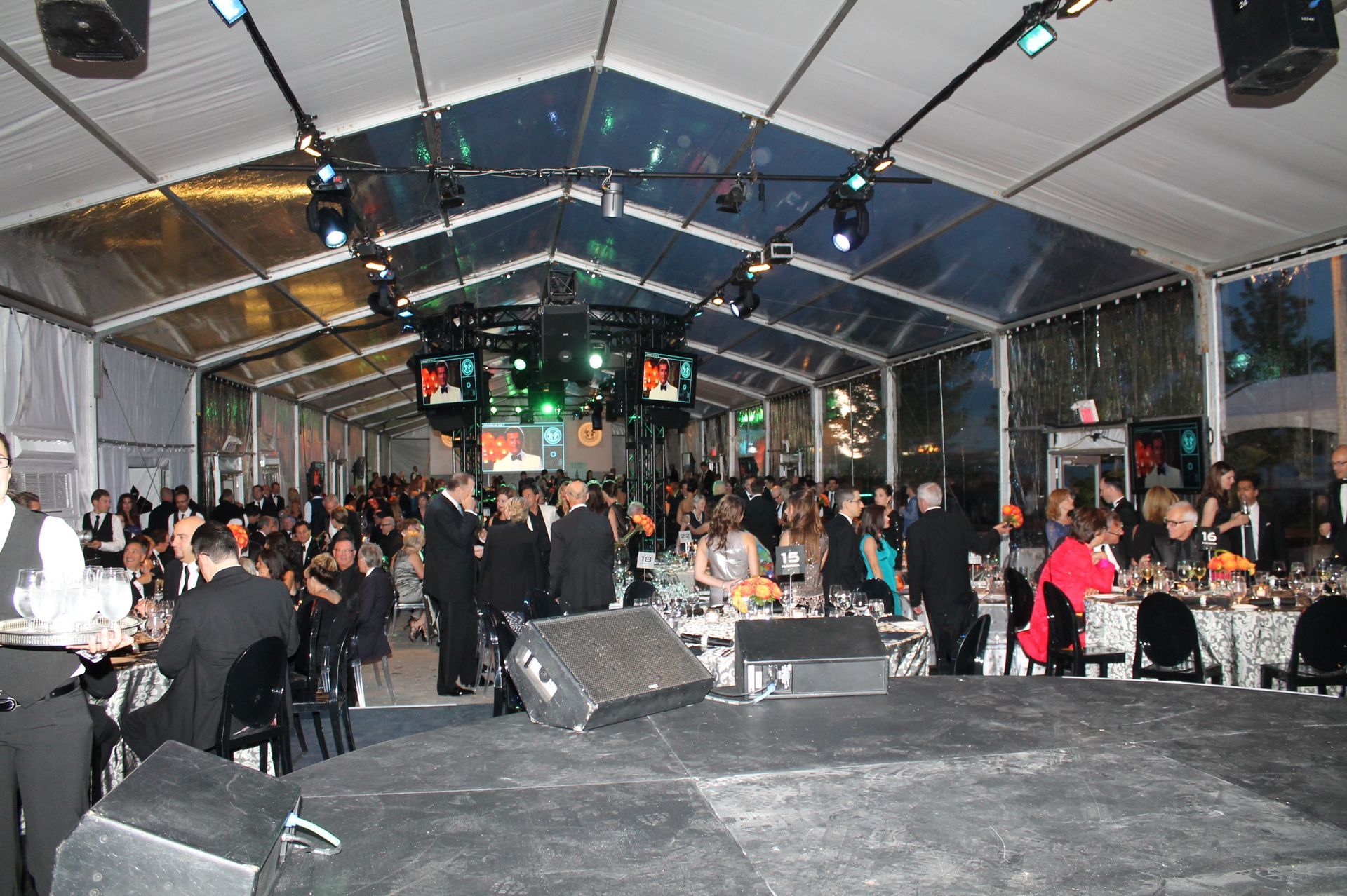 Large event tent with people, stage in foreground, lights overhead.