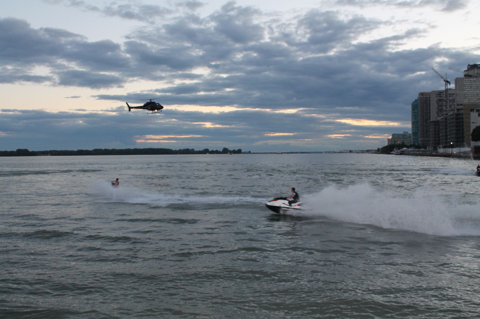 Watercraft and helicopter over water near a city at dusk.