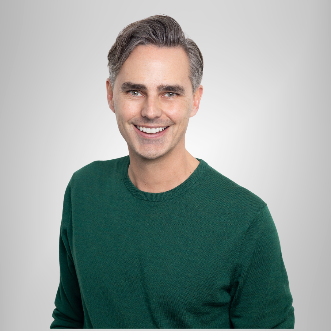 A man in a green sweater is smiling for the camera.