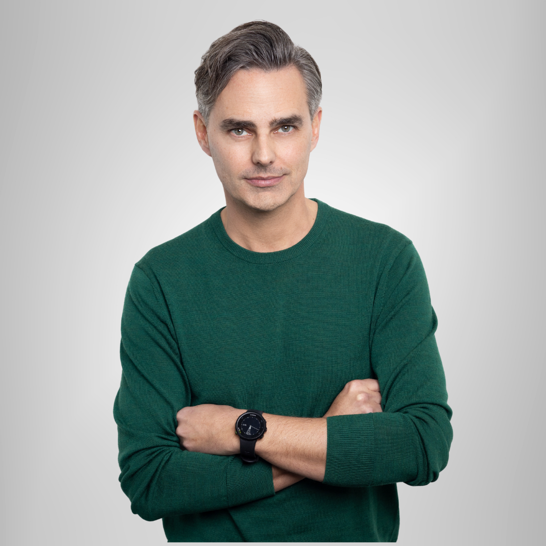 Man in a green sweater with arms crossed against a light gray background.
