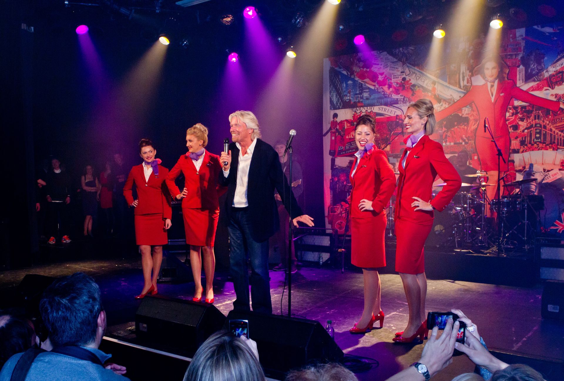 A group of people are standing on a stage with a man standing in front of a microphone.