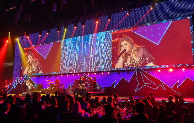 A woman is singing into a microphone on a stage in front of a large screen.