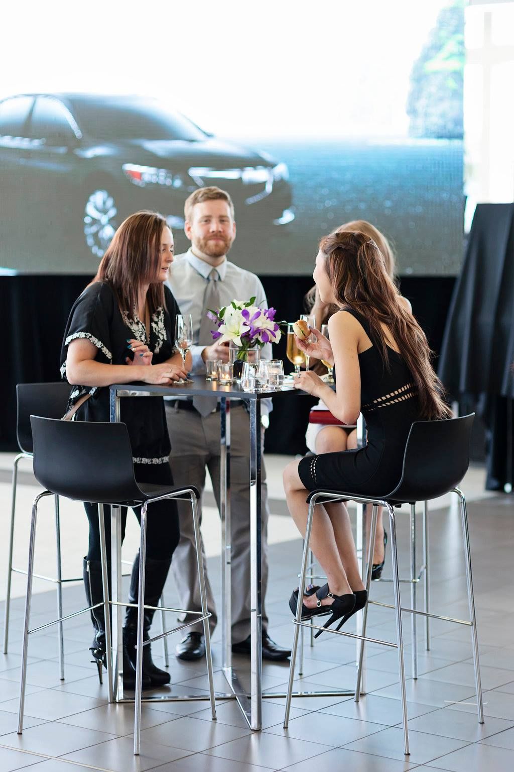 A group of people are sitting around a table with a car in the background.