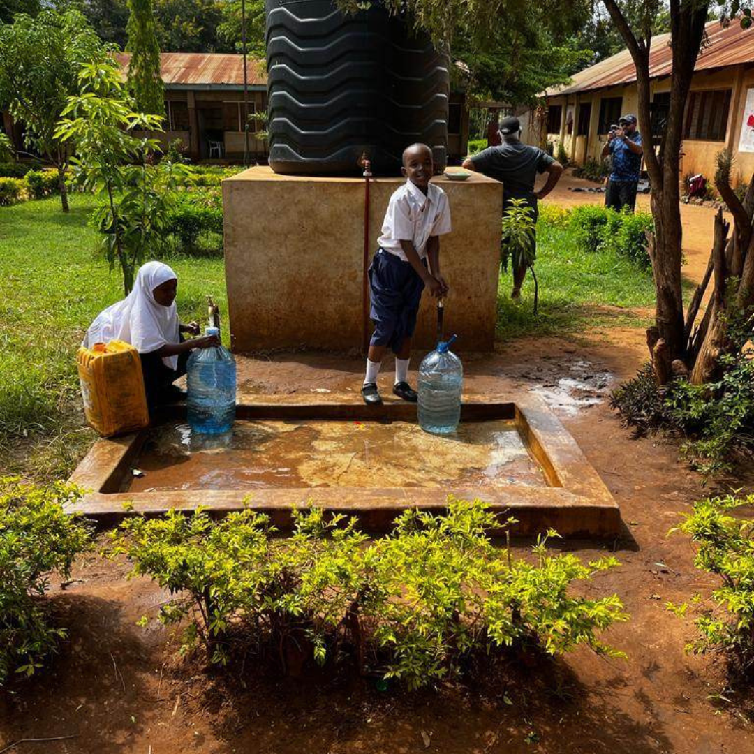 A man is holding a bottle of water in front of a water tank