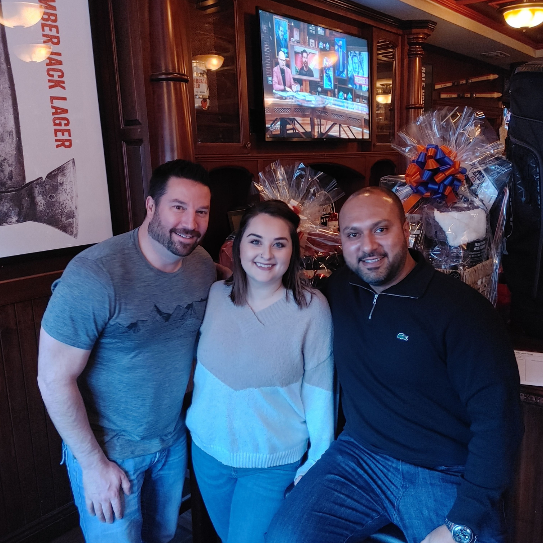 Three people posing for a picture in front of a sign that says lager