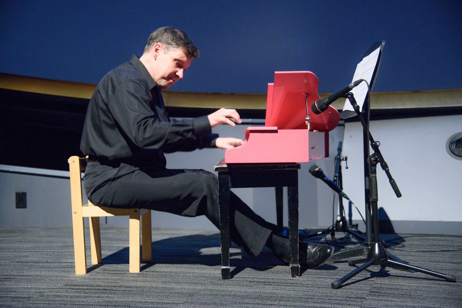 A man in a black shirt is playing a red piano