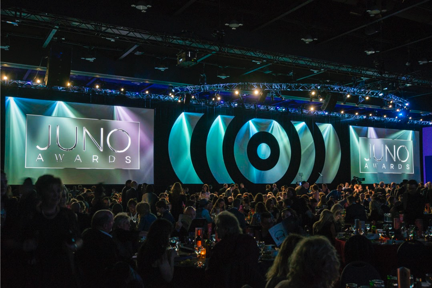 A large group of people are sitting at tables in front of a large screen that says juno awards