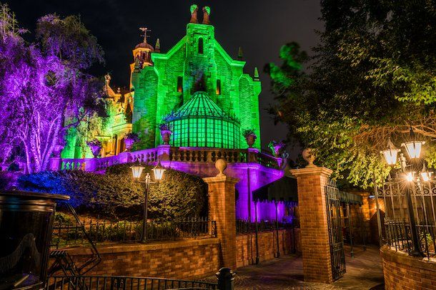 A haunted mansion is lit up with green and purple lights at night.