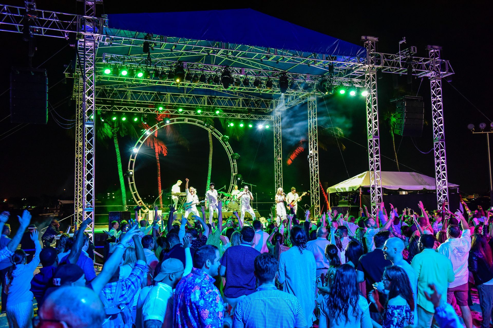 Two robot performers with lights dance at a party with people in white clothing.