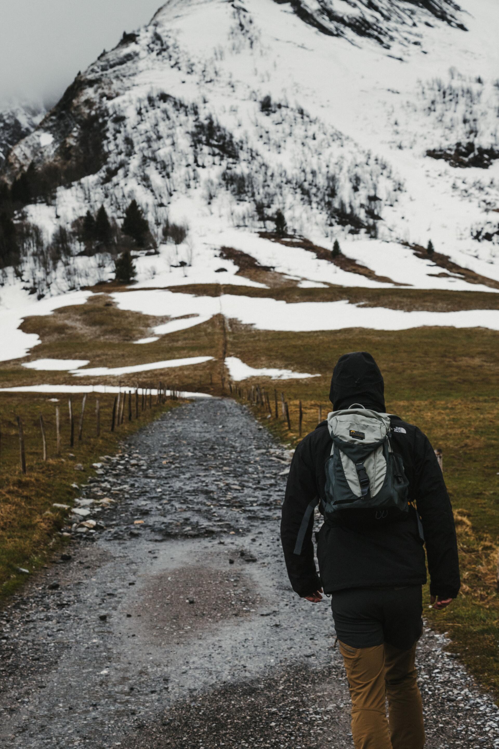 A person with a backpack is walking down a path in the mountains.