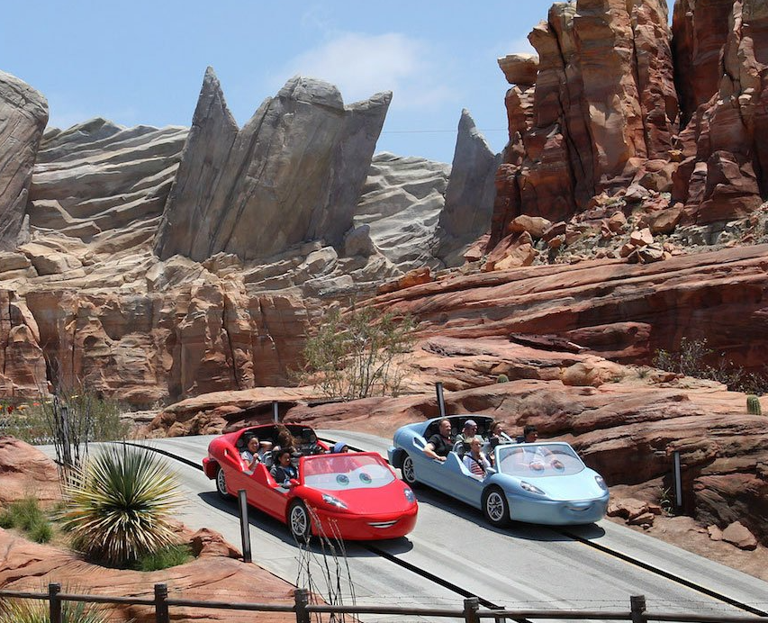 Two cars are driving down a road with rocks in the background