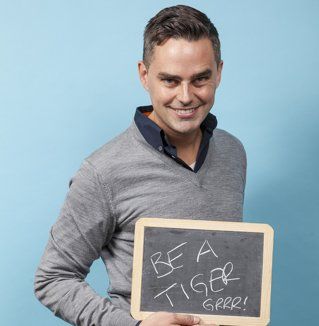 A man is holding a sign that says be a tiger grrr