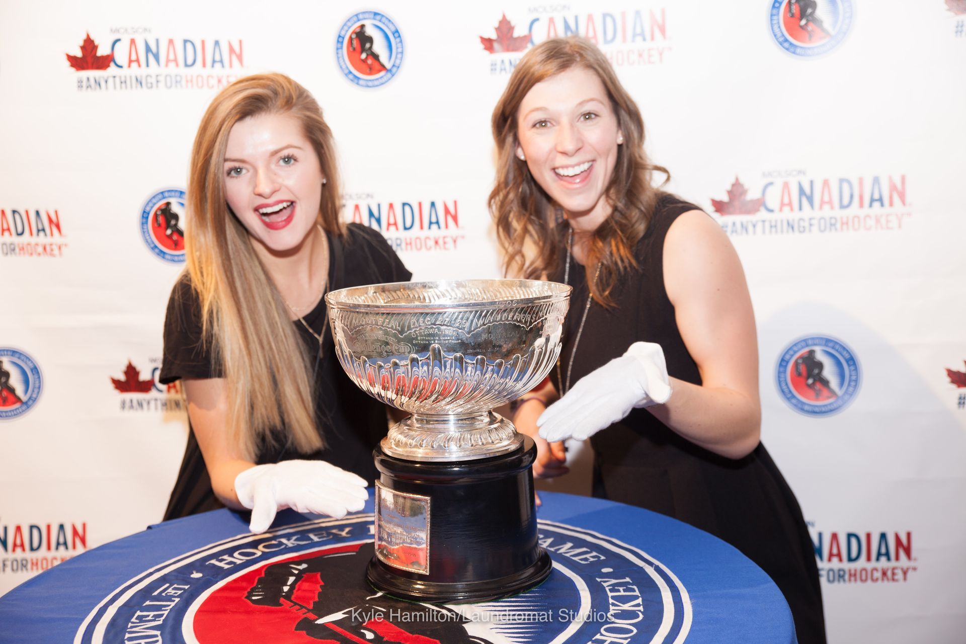 Two women are standing next to a trophy on a table.