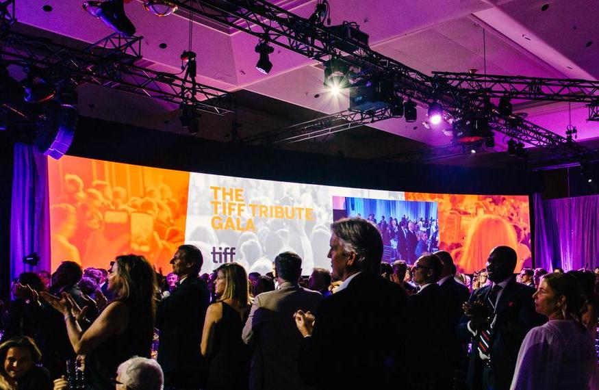 A large group of people are dancing in a large room at a gala.