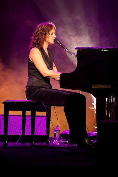 A woman is sitting at a piano and singing into a microphone.
