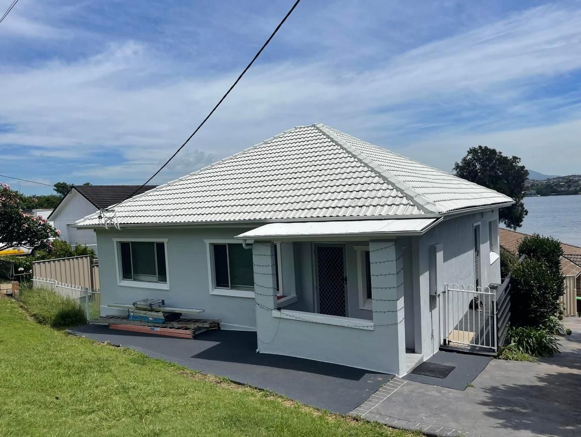 A Small White House With A White Roof Is Sitting On Top Of A Hill — APEX Painting & Maintenance In Primbee, NSW