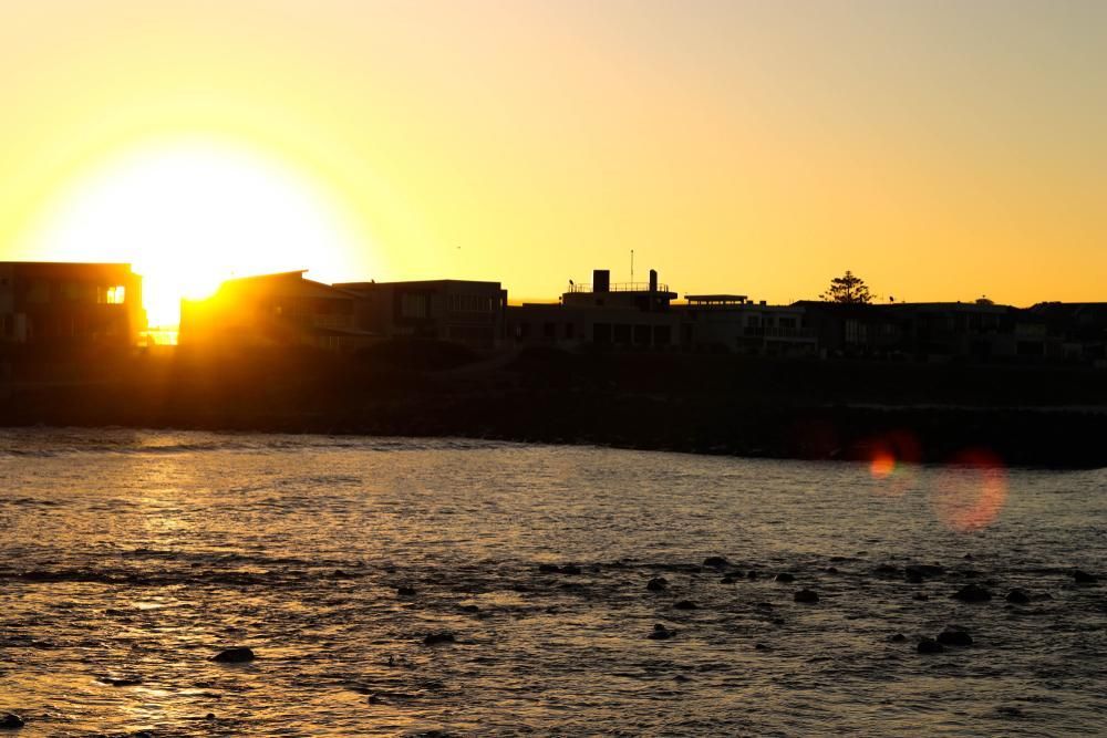 The Sun Is Setting Over A Body Of Water With A City In The Background — APEX Painting & Maintenance In Shellharbour, NSW