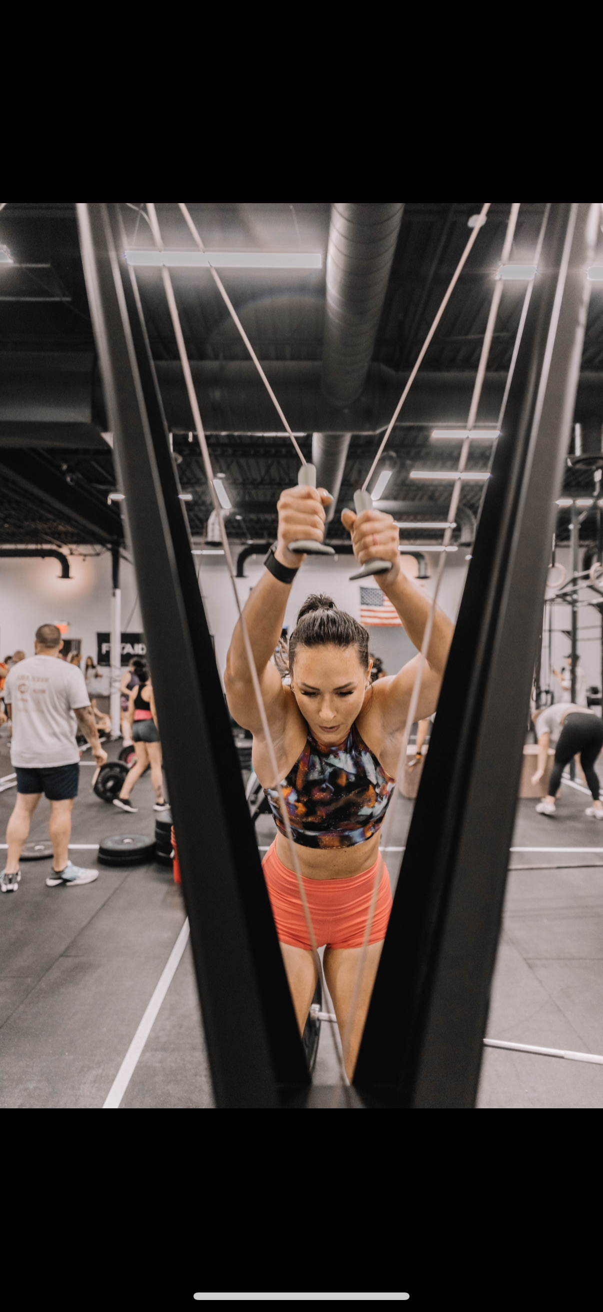 Woman performing a cable machine exercise in a gym, wearing an orange outfit.