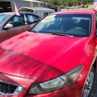 Red sedan with a glossy hood parked outdoors, with a silver car beside it.