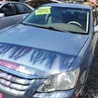Blue sedan parked outdoors with a yellow windshield sign and tree shadows across the hood