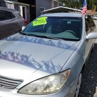 Silver sedan with a neon green sale sign in the windshield, parked outside a house with an American flag.