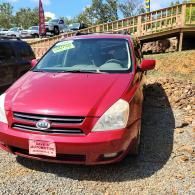 Red minivan parked on a gravel driveway beside a wooden bridge in bright sunlight