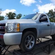 Silver pickup truck parked on a car carrier trailer outdoors under a blue sky