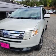 White Ford SUV parked on a gravel driveway beside a house, with a pink license plate cover.