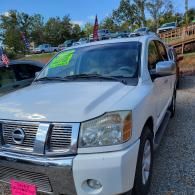 White Nissan SUV parked outdoors on gravel, with a bright green windshield sale sign.