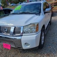 White Nissan pickup truck parked on gravel, front view with chrome grille and bright pink license plate cover