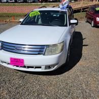 White sedan parked outdoors with a pink license plate and a person leaning out the sunroof