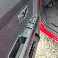 Close-up of a car driver’s door panel with window controls and a red exterior door edge.