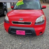 Red Kia parked on gravel with a pink sale sign on the front plate area