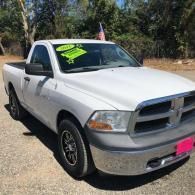White pickup truck parked outdoors with a bright green windshield sale sign and pink front plate cover