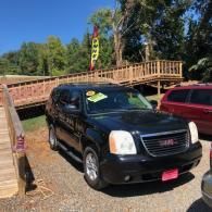 Black SUV parked outdoors beside a wooden bridge on a sunny day.