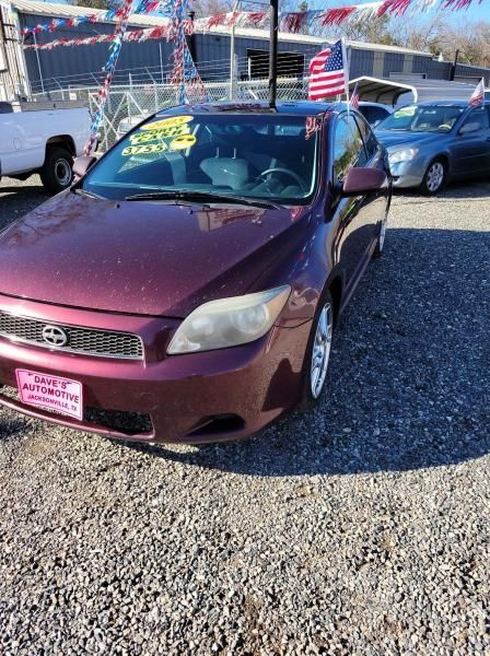 Maroon sedan parked on gravel at a car lot with a blue car behind it.