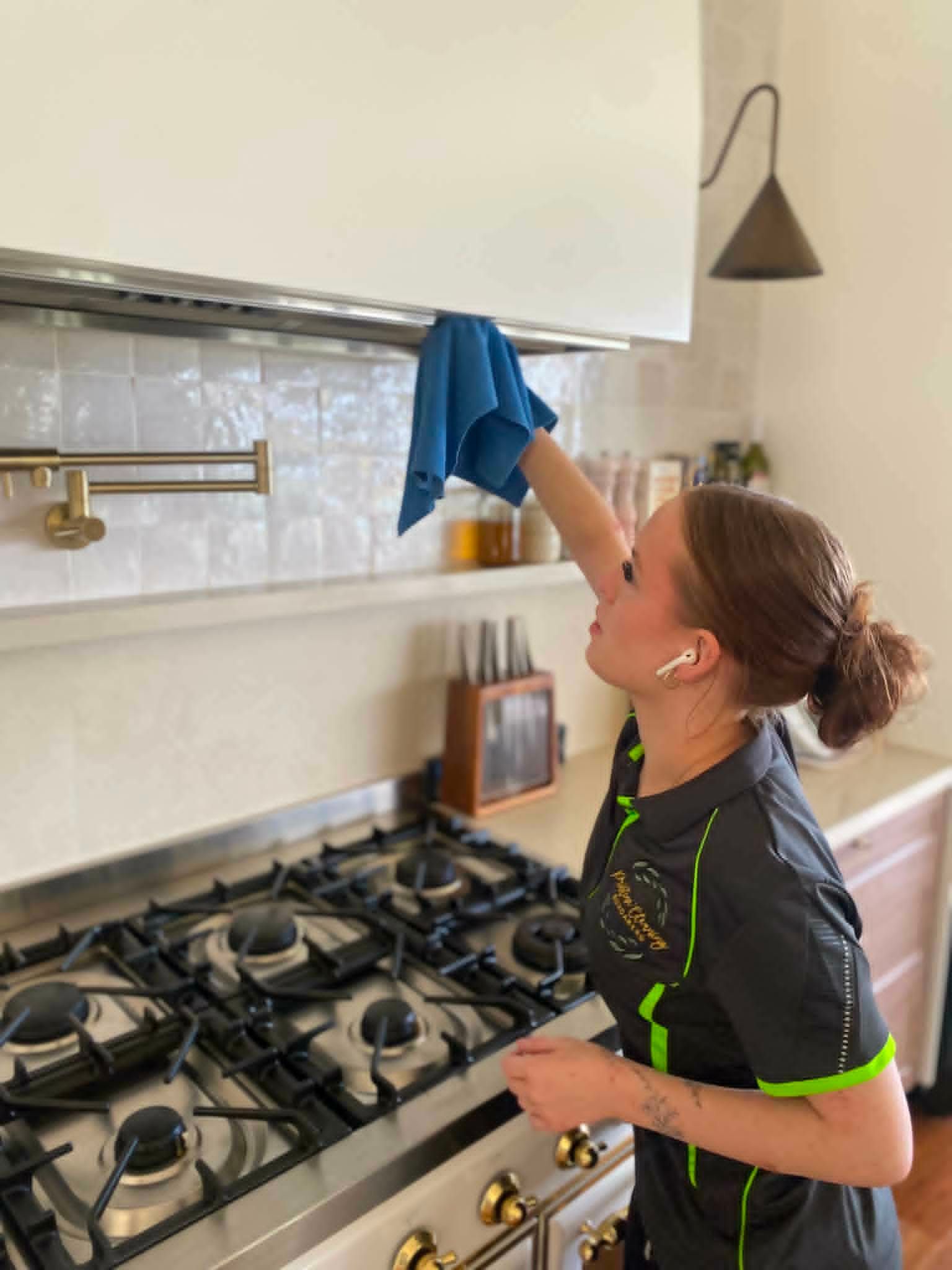 Person cleaning a kitchen cabinet with a blue cloth beside a gas stove