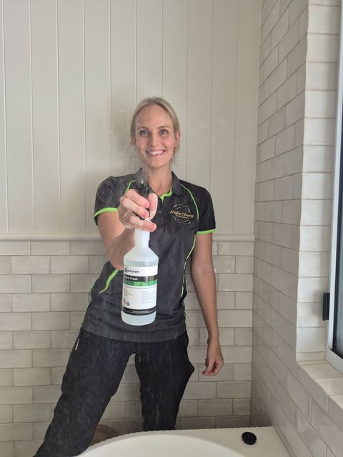 Person smiling and holding a spray bottle on a porch against a white paneled wall