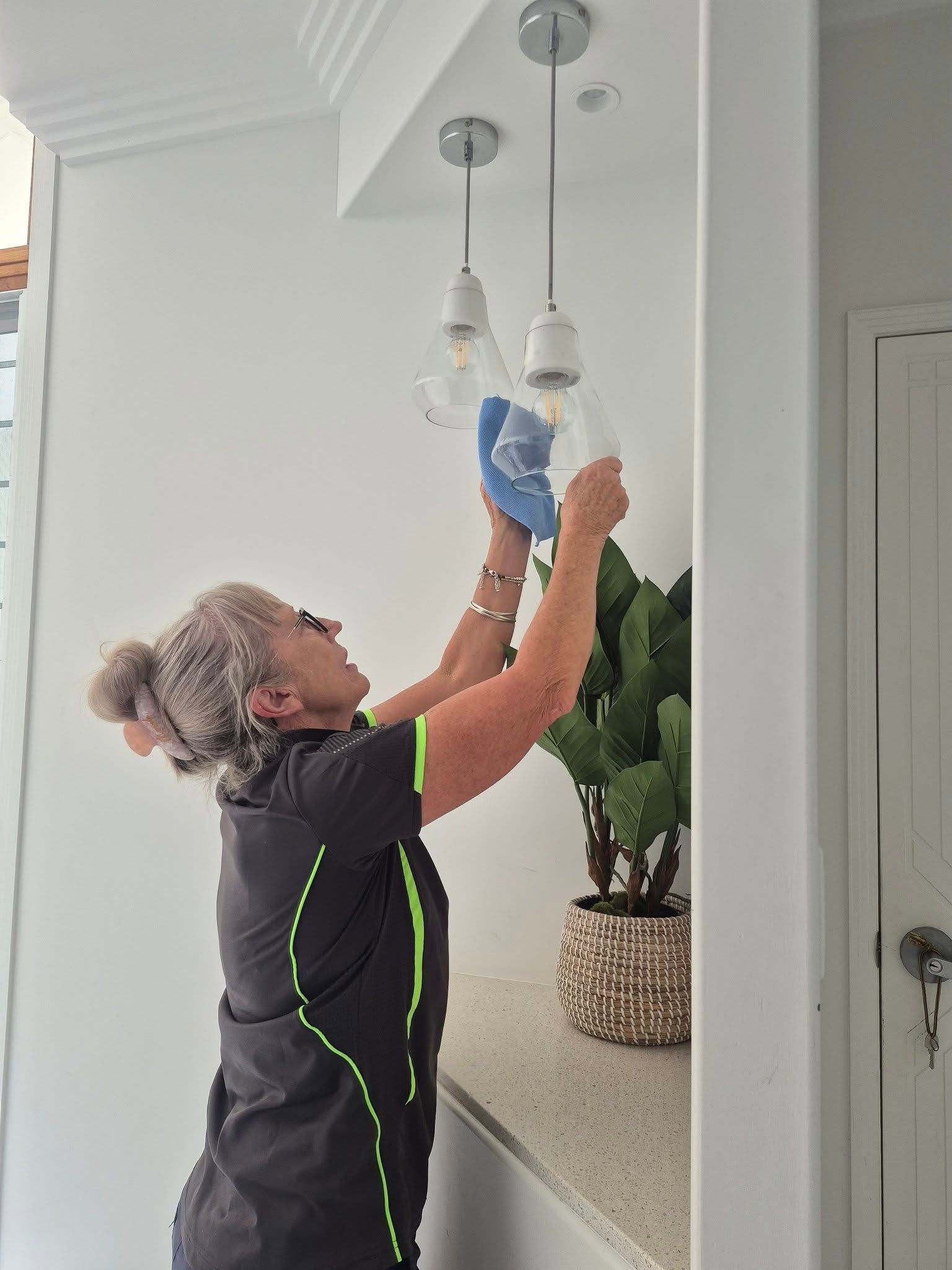 Person Cleaning a Hanging Light Fixture With a Cloth in a Bright Kitchen — Pristine Cleaning Bundaberg In Kalkie, QLD