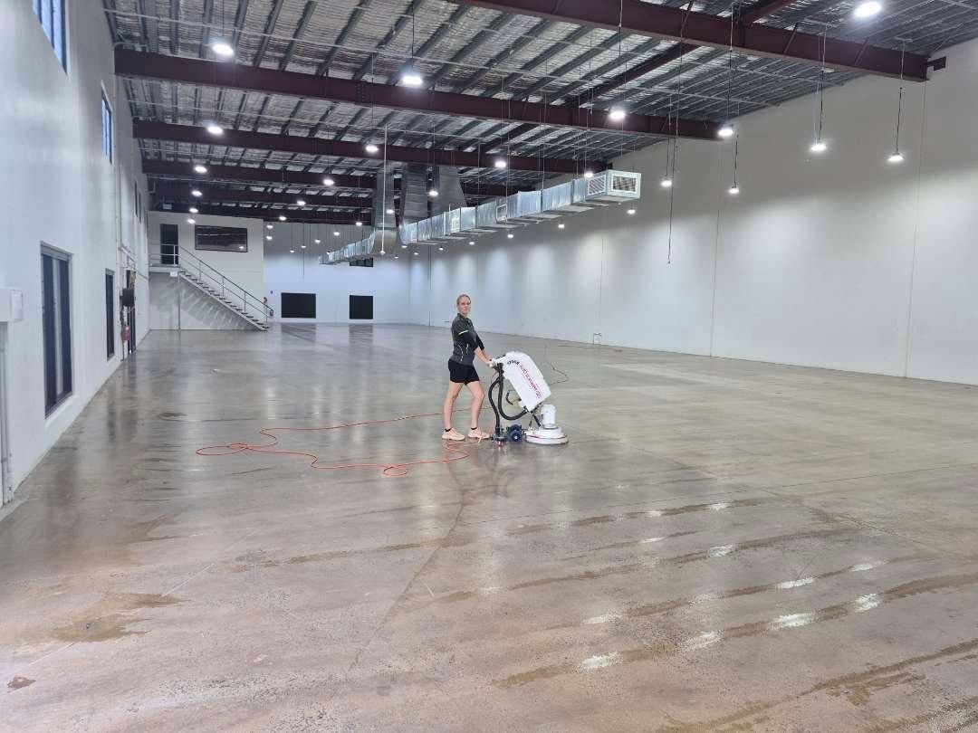 Empty Warehouse With a Person Cleaning a Wet Concrete Floor — Pristine Cleaning Bundaberg In Kalkie, QLD