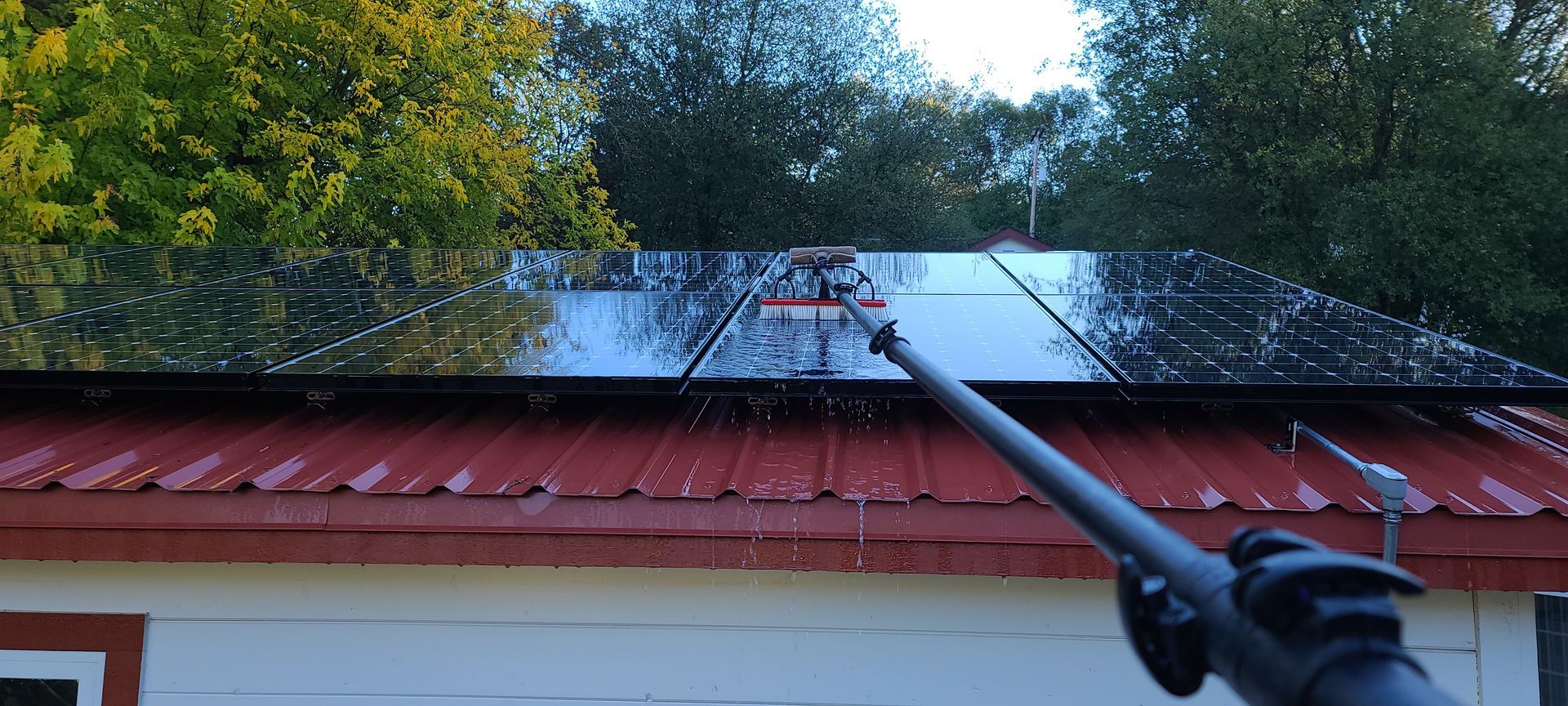 A person is cleaning a solar panel on the roof of a house.