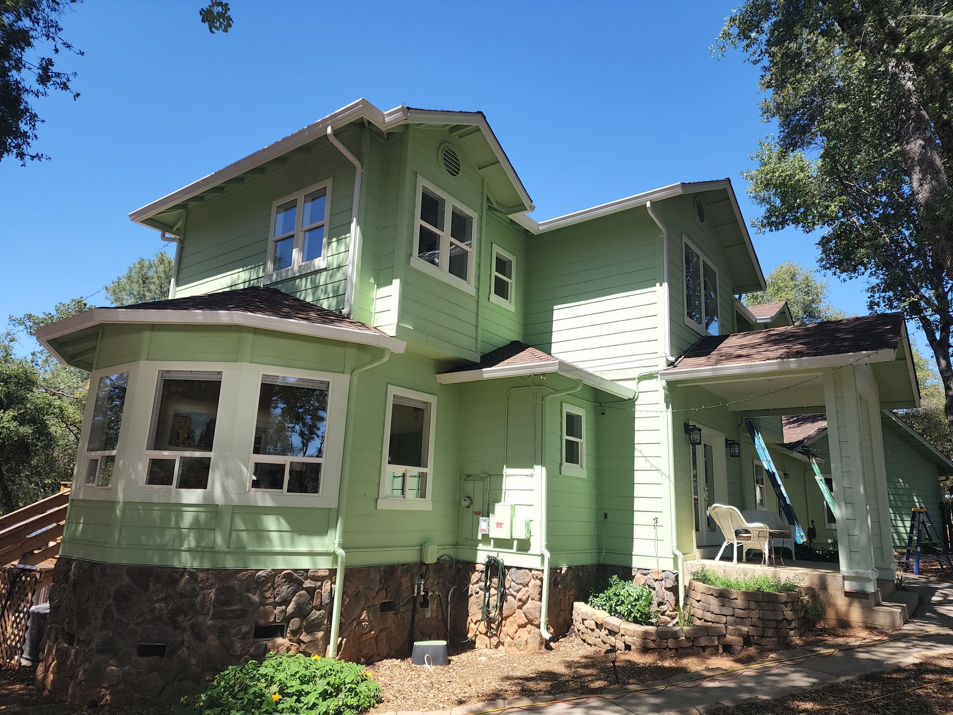 A large green house with a porch and a blue sky in the background.