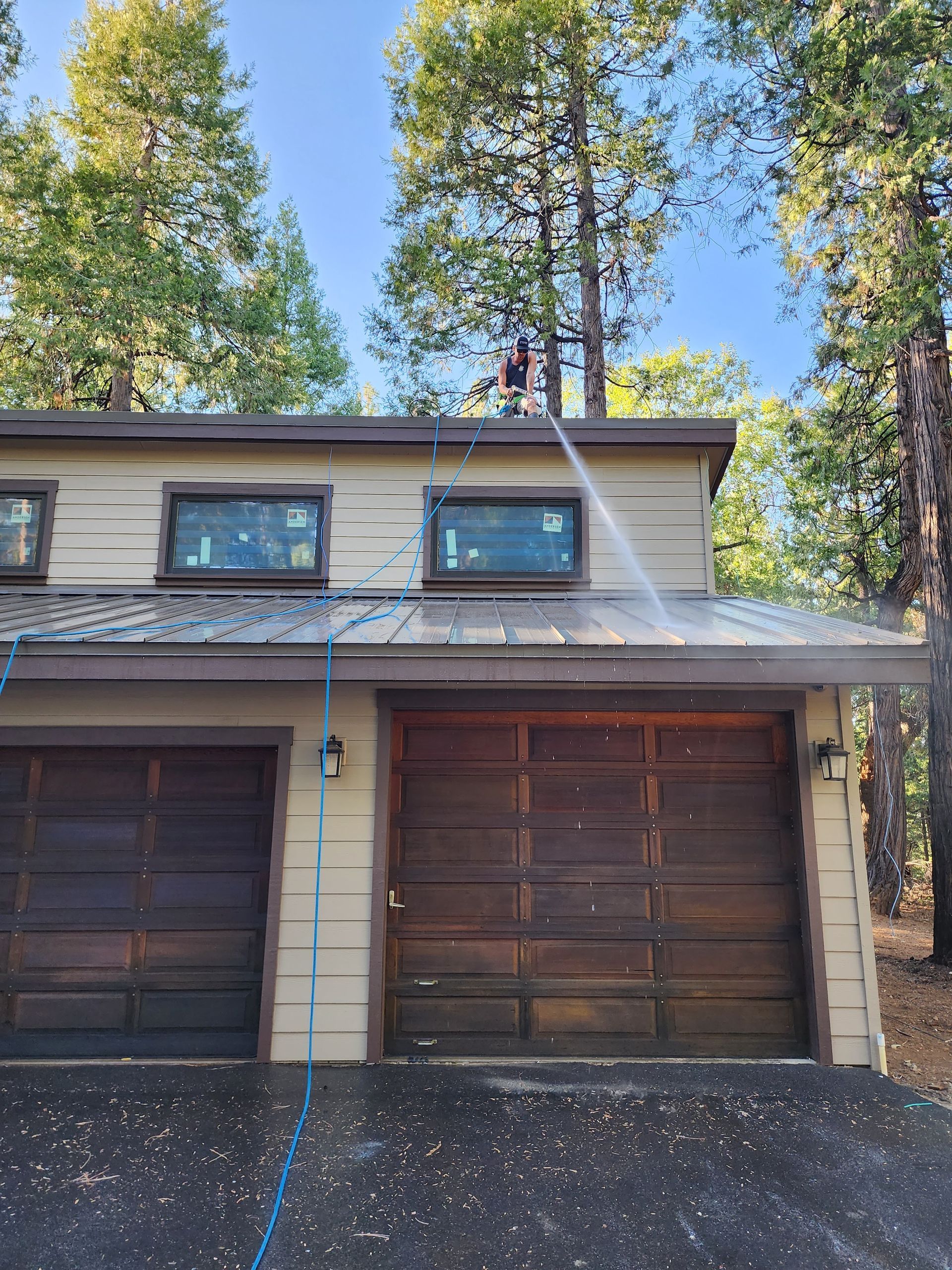 A man is cleaning the roof of a house with a pressure washer.