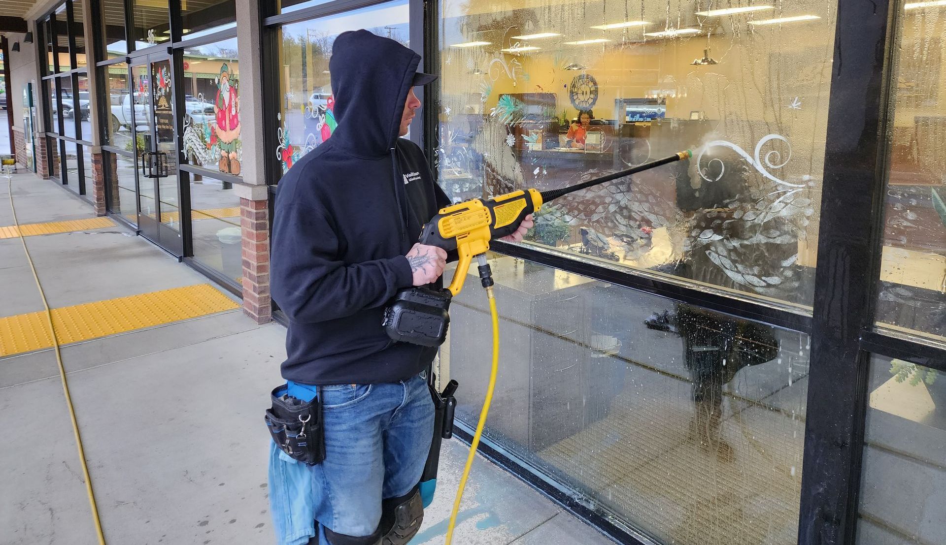 A man is cleaning a store window with a high pressure washer.