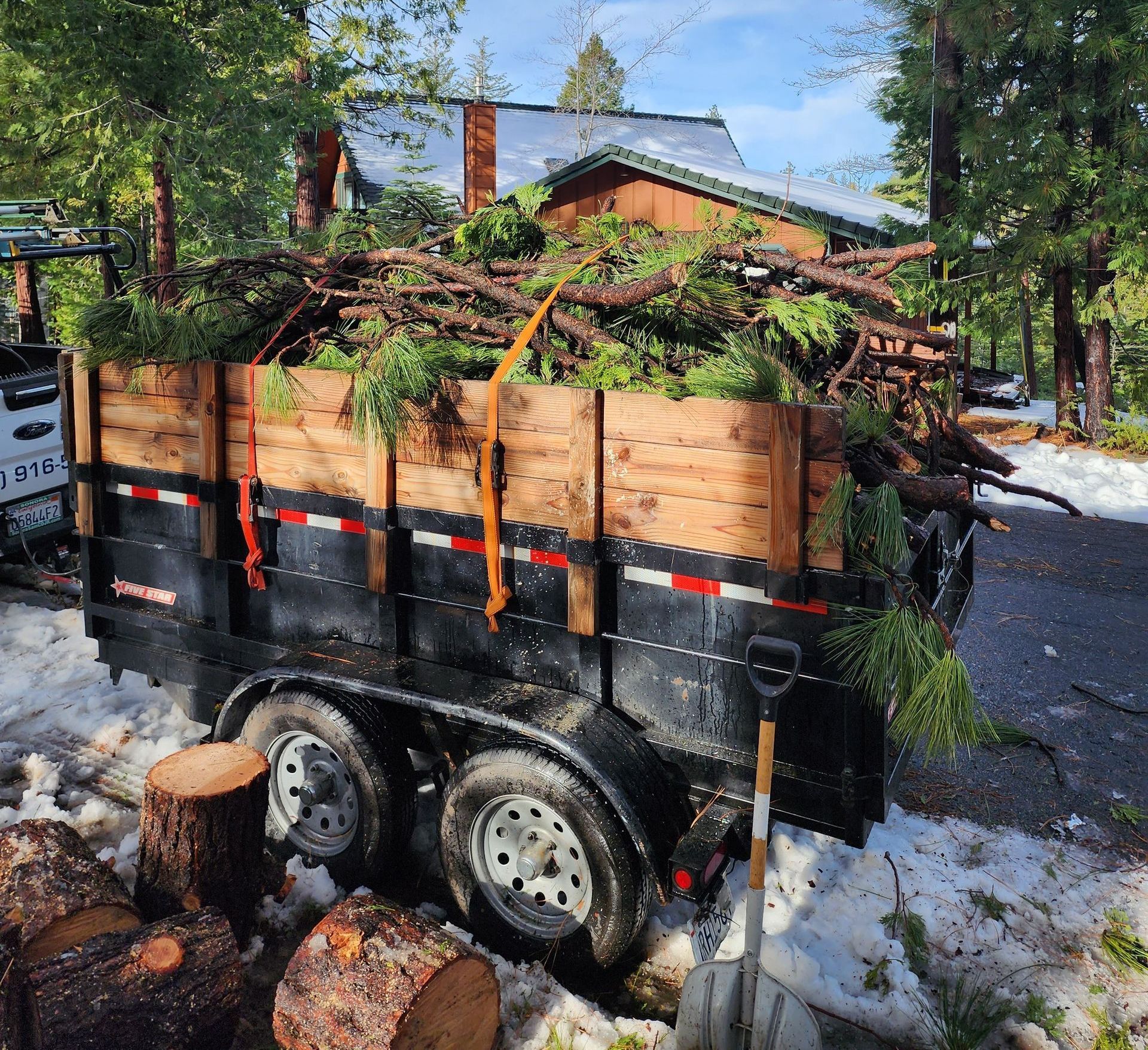 A trailer filled with logs is parked in front of a house.