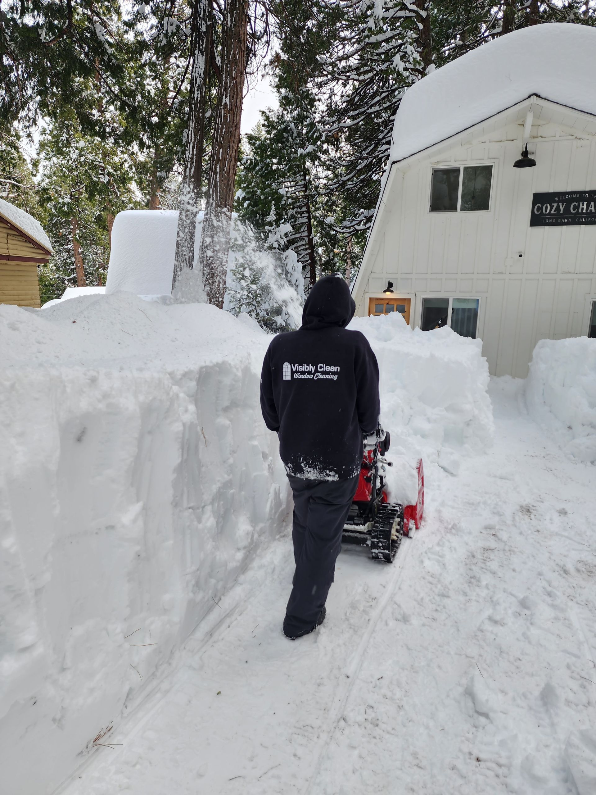 A man is pushing a snow blower down a snow covered road.